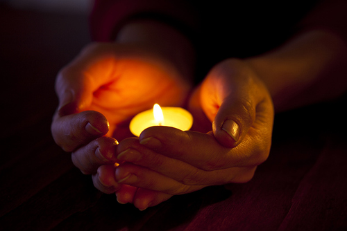 Hände halten eine Kerze im Gebet.