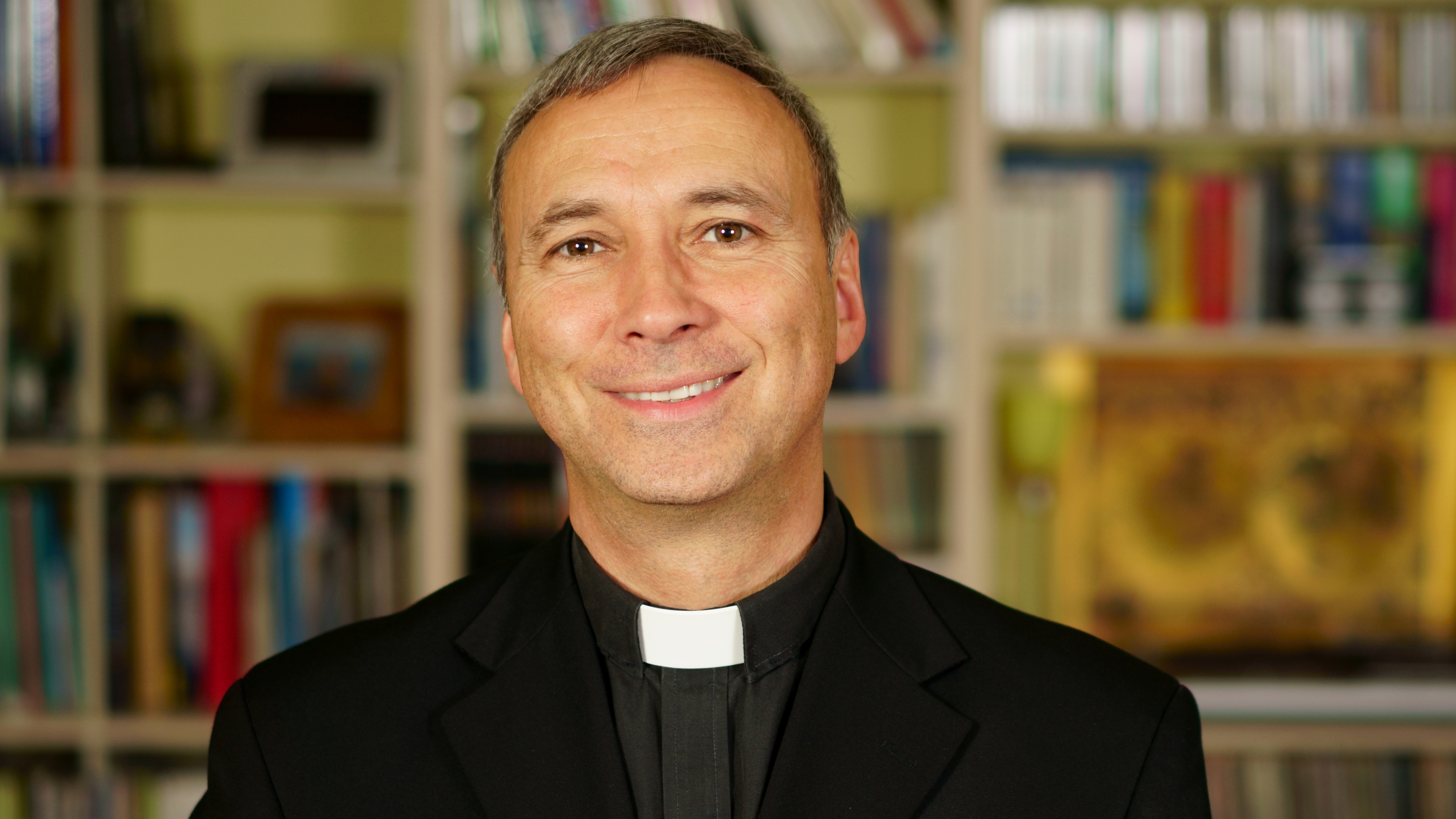 A portrait of a good looking serious catholic priest.  He looks at us with interest, pensiveness, proselytising, joy, happyness, trust and peacefulness.